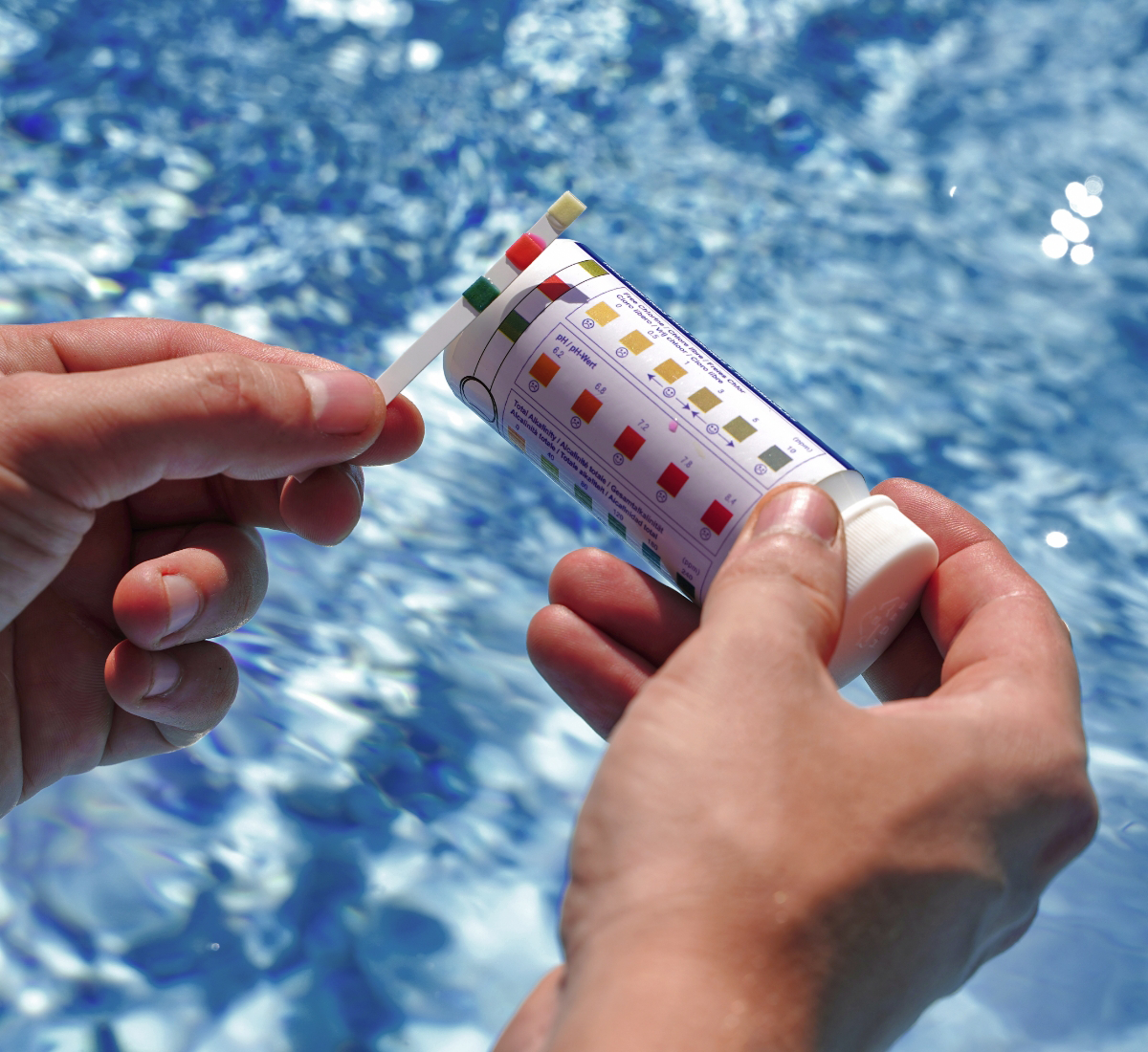 A person holding a pool water test strip and container above a body of water, ensuring pristine conditions in line with top-quality pool maintenance services.