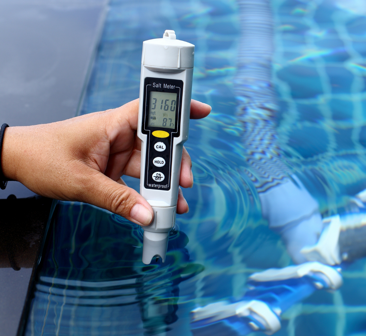 A hand holds a salt meter, assessing the salinity levels of the pool with precision—an essential step in maintaining pristine waters for top-notch pool cleaning services.