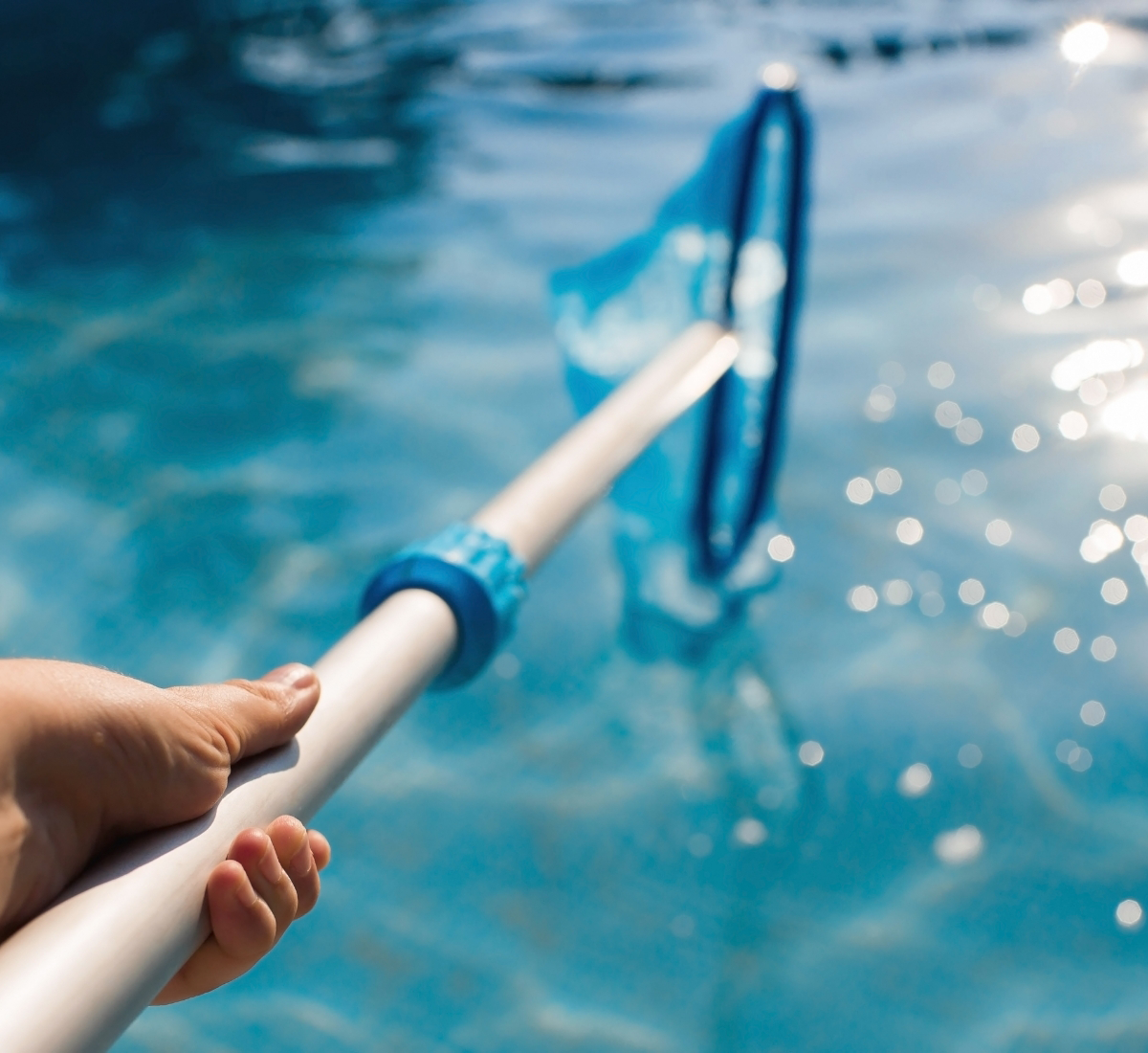 A hand holding a pool net over the water, skimming the surface on a sunny day.