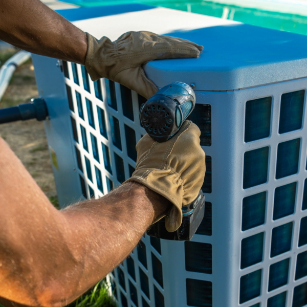 Person wearing gloves using a power drill on an outdoor pool unit.